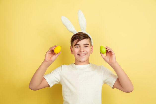 兔子微笑找蛋来了白人男孩作为一个复活节兔子在黄色的工作室背景复活节快乐的问候美丽的男模人类情感的概念 面部表情 节日复制空间漫画鸡蛋耳朵