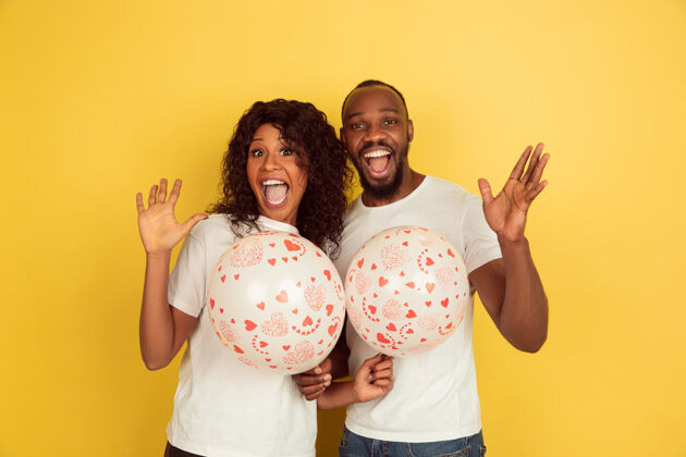 在一起手持气球情人节庆典 黄色工作室背景上的一对快乐的非洲裔美国夫妇人类情感的概念 面部表情 爱情 关系 浪漫的节日情侣亲吻微笑