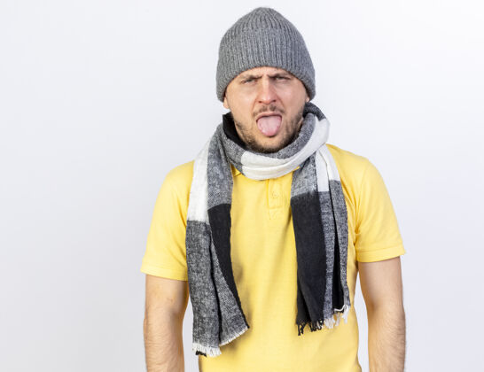 舌头恼怒的年轻金发病斯拉夫男子戴冬季帽子和围巾stucks出舌头隔离在白色墙壁与复制空间疾病金发穿