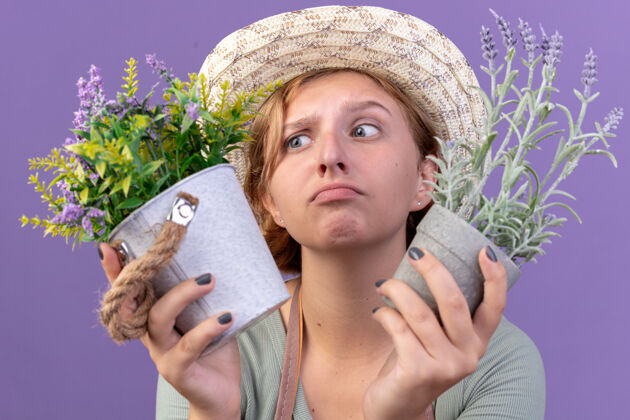 花盆困惑的年轻斯拉夫女园丁戴着园艺帽拿着紫色花盆里的花女性花园艺