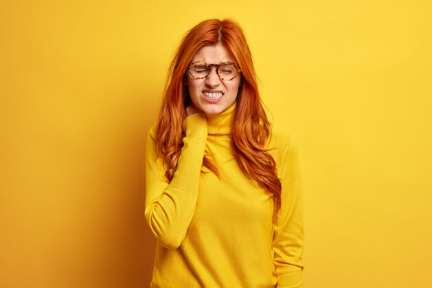 眼镜红发不高兴的女人摸脖子感觉强烈疼痛有办公室综合症导致久坐的生活方式戴眼镜高领毛衣人类紧张伤害