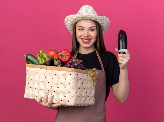 花园笑容可掬的白人女园丁 戴着园艺帽 手里拿着菜篮子和粉红色的茄子篮子茄子蔬菜