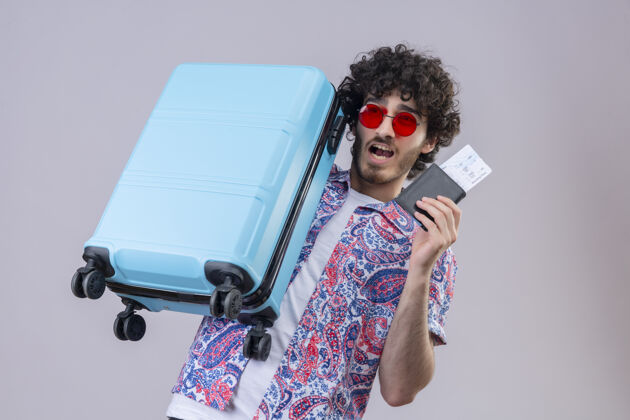 旅行者快乐的年轻英俊的卷发旅行者戴着太阳镜拿着机票 钱包和手提箱在与世隔绝的空白处与复印空间机票持有太空