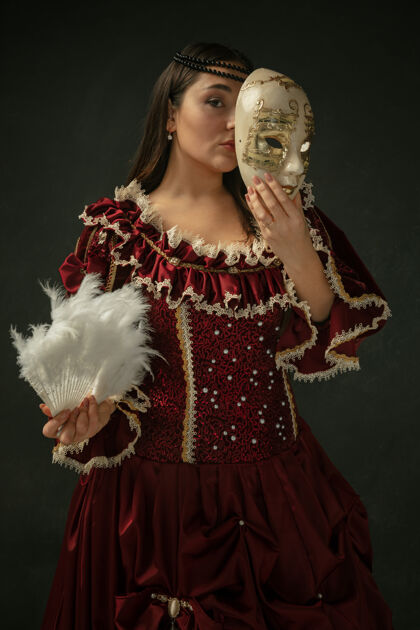 时代戴着面具藏起来穿着红色复古服装站在深色背景上的中世纪年轻女子肖像女模特是公爵夫人 皇室成员时代 现代 时尚 美丽的比较概念公主帽子头发