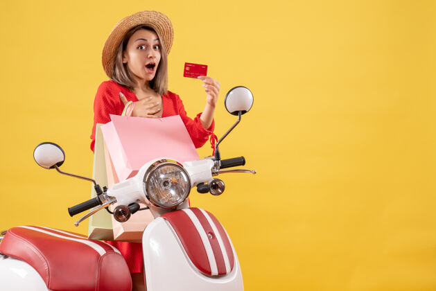 购物正面图是一位穿着红色连衣裙 手持购物袋和购物卡的快乐女士身体轻便摩托车前面