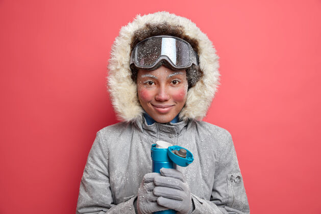 季节活跃的女性滑雪板运动员穿着温暖的外套 皮肤发红 脸冻在寒冷的冬天喝热水瓶里的热饮料人冰冻欢呼