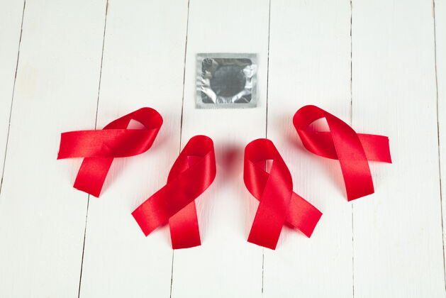 日艾滋病宣传标志红色丝带 白色木桌子背景 带避孕套世界艾滋病日概念健康 帮助 关怀 支持 希望 疾病 保健概念运动世界意识