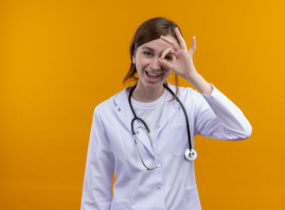 医生快乐的年轻女医生穿着医用长袍和听诊器在孤立的橙色空间和复印空间做着看手势穿橙色女性