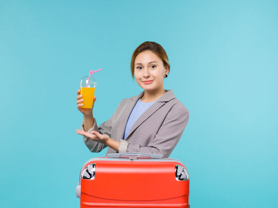 果汁前视图女性在度假与她的红色袋子举行的蓝色背景度假飞机旅行海上旅行新鲜果汁微笑旅行前面