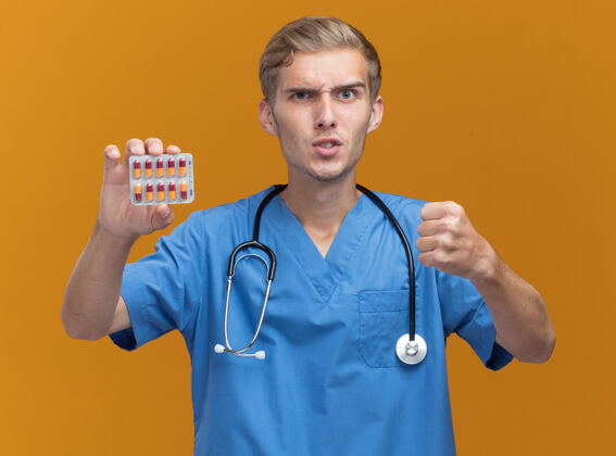年轻人年轻的男医生穿着医生制服 手持听诊器 把药片隔离在橙色的墙上感觉抱着脸