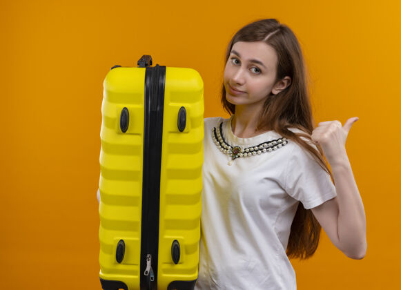 手提箱自信的年轻旅行家女孩拿着手提箱 指着右边孤立的橙色空间侧线橙色旅行者