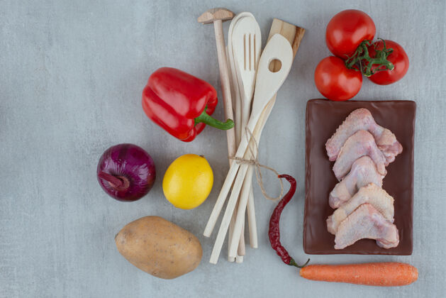 工具蔬菜 厨房用具和生鸡翅在灰色的表面上番茄胡萝卜生的