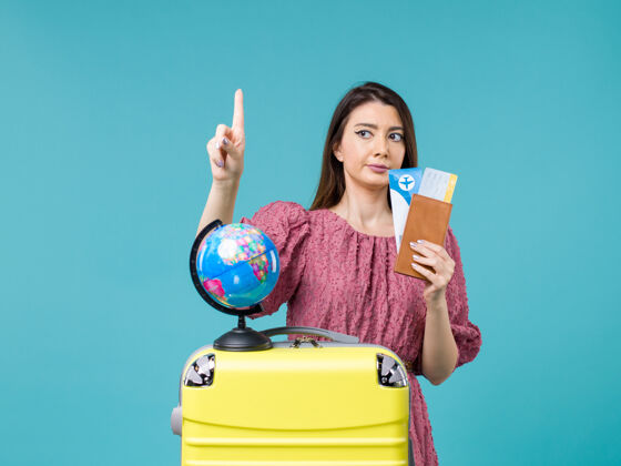 蓝色前视图女性在旅行中拿着她的机票在蓝色背景海上旅行女性旅行度假之旅假期票举行