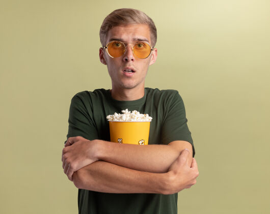 姿势一个穿着绿衬衫戴着眼镜的年轻帅哥抱着橄榄绿墙上一桶爆米花感觉表情男人