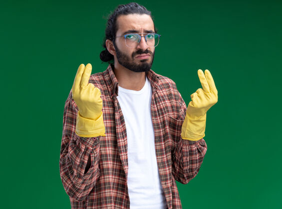 姿势悲伤的年轻帅气的清洁工 穿着t恤 戴着手套 在绿色的墙上显示着小费的姿势悲伤手势清洁