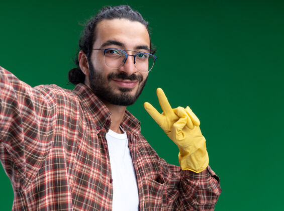人高兴的年轻帅气的保洁员穿着t恤 戴着手套 举着和平的姿态孤立在绿色的墙上脸抱着年轻