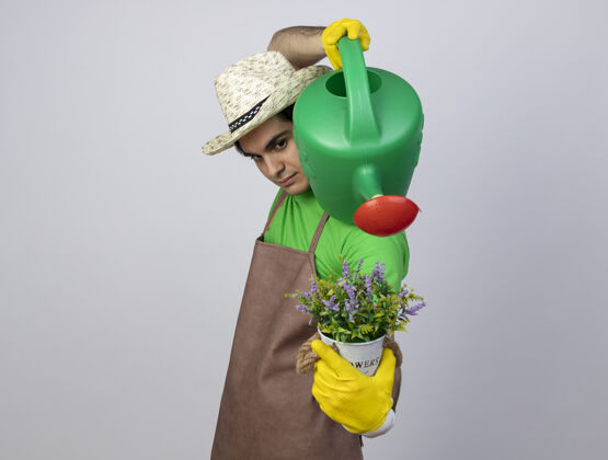 小伙子自信的年轻男园丁穿着制服戴着园艺帽和手套在花盆里用水壶浇花手套男穿
