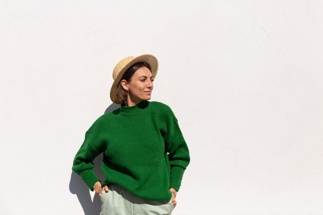 脸穿着绿色休闲毛衣和帽子的时髦女人在户外白墙上欢快 快乐 兴奋地享受炎炎夏日城镇女性旅程