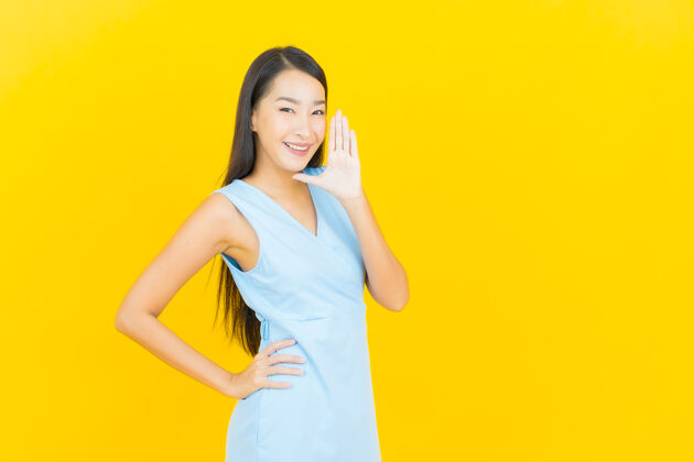 快乐在黄色墙壁上描绘美丽的亚洲年轻女子微笑的动作穿着五颜六色颜色