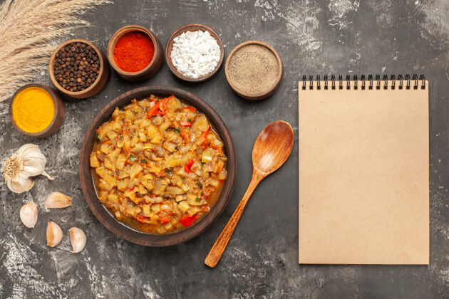 蔬菜顶视图烤茄子沙拉碗不同的香料碗大蒜笔记本在黑暗的表面食物一餐木勺