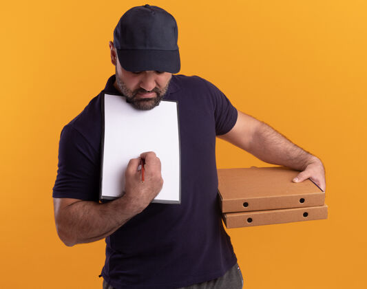 脸一个穿着制服 戴着帽子的中年送货员拿着披萨盒 在黄色墙上的剪贴板上写着什么盒子人拿着