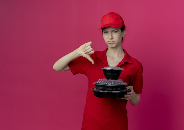 深红色年轻漂亮的送货女孩 穿着红色制服 戴着帽子 拿着食物容器 拇指朝下 在深红色背景下 留着复印空间女孩拇指帽子