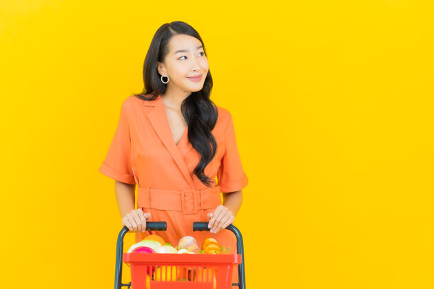 年轻肖像美丽的亚洲年轻女子微笑着从黄色超市购物篮零售亚洲产品