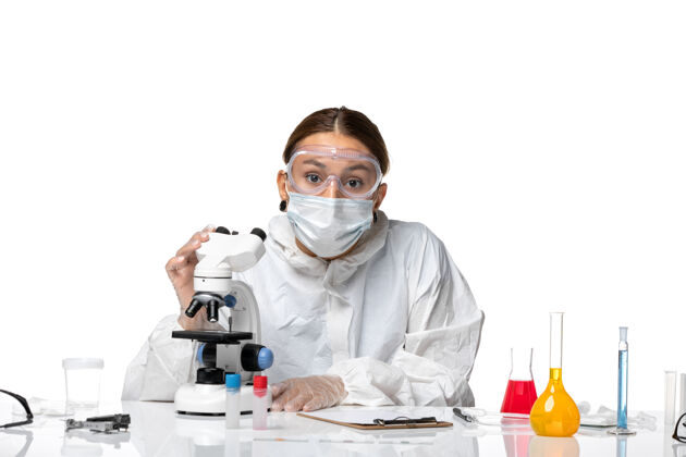 药品前视图：女医生穿着防护服 戴着口罩 用显微镜观察一种白色背景的健康冠状病毒大流行专业实验室外套女医生