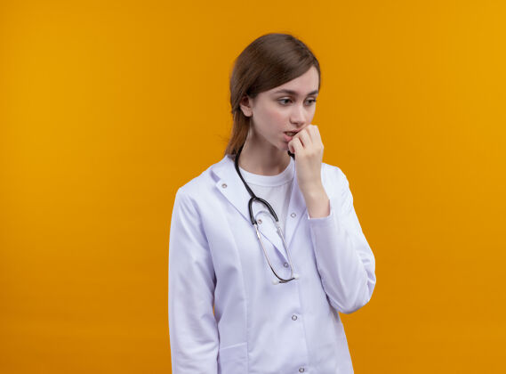 复制焦急的年轻女医生穿着医用长袍 戴着听诊器 手放在嘴唇上 隔离着橙色的空间和复印空间手医生太空