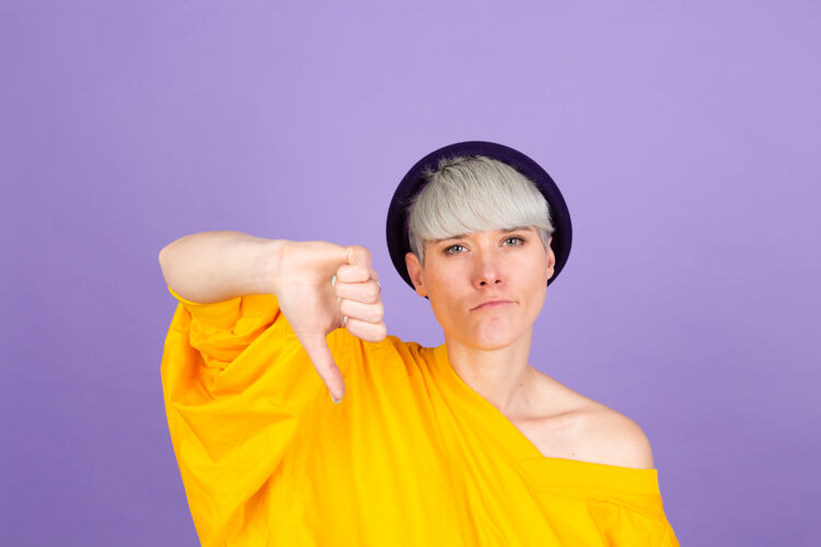 消极紫色墙上的时髦的欧洲女人看起来不开心和生气 表示拒绝和否定 大拇指朝下表情不好模特复制空间不高兴