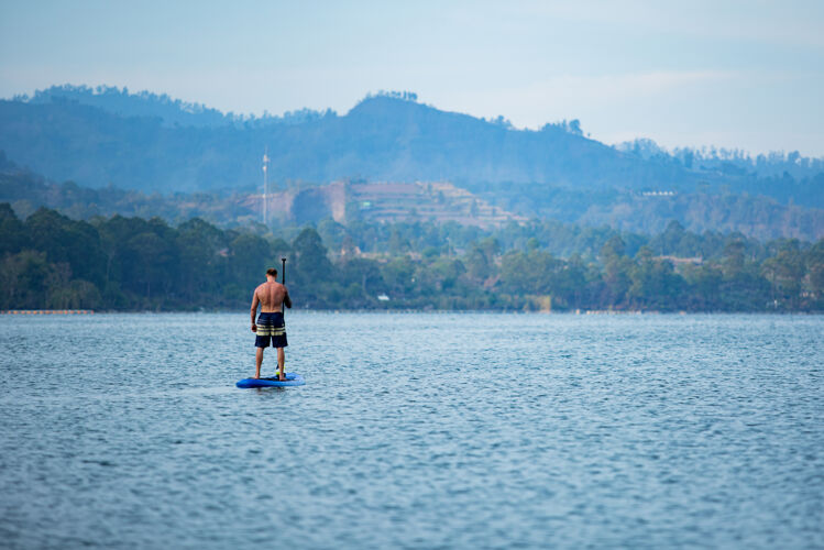 海滩一个男人在湖边骑冲浪板划桨热带娱乐