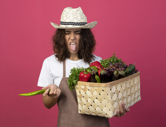 胡椒穿着制服的年轻女园丁 戴着园艺帽 手里拿着一个有胡椒粉的菜篮子 舌头呈粉红色粉色不愉快显示