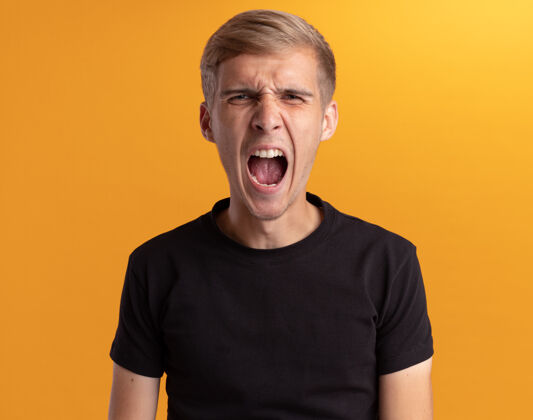 愤怒愤怒的年轻帅哥穿着黑衬衫隔离在黄色的墙上穿帅哥年轻