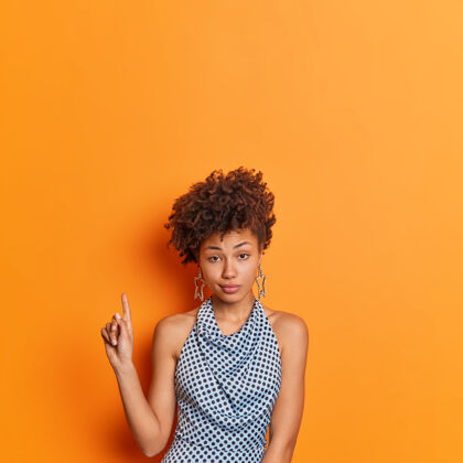 折扣严肃时尚的年轻非洲裔美国妇女在时尚的波尔卡圆点服装表明上述复制空间给出了生动的橙色背景下的建议姿势只要看看这个报价手指建议人