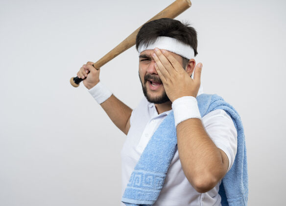 年轻未被释放的年轻运动男子戴头带和手环与毛巾在肩上提出棒球棒覆盖的脸与手隔离在白色墙壁与复制空间头带男人穿