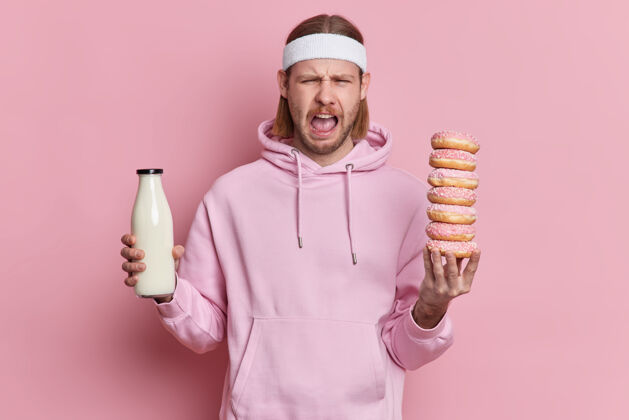 一个愤怒的运动员手里拿着一堆甜甜圈和一瓶牛奶 满脸笑容心烦堆运动衫