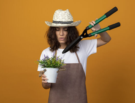 花盆年轻的女园丁穿着制服 戴着园艺帽 用剪子在花盆里切花女人切割人
