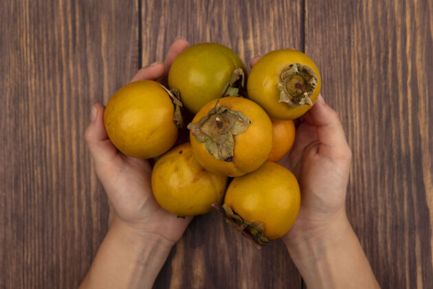 新鲜女性手拿新鲜的橙色柿子水果放在木桌上的俯视图雌性柿子食物