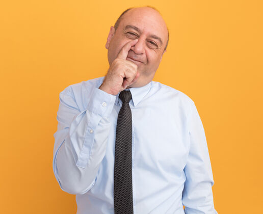 中年人一个戴着领带的白色t恤的中年男子把手指放在鼻子上 隔离在橙色的墙上手指领带男人