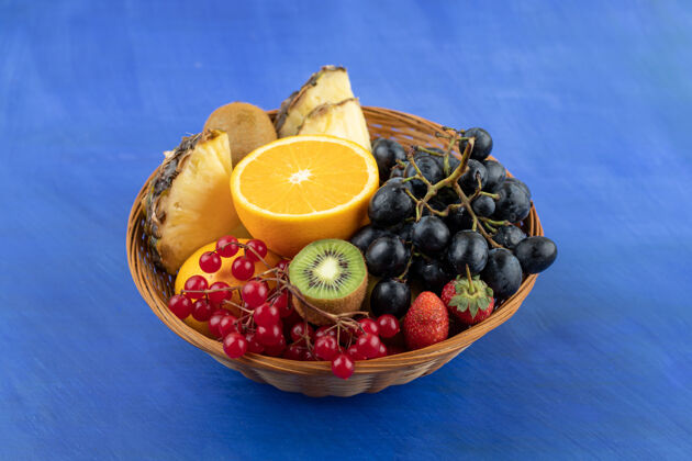葡萄一个装满水果的柳条篮子在蓝色的表面上柳条美味浆果