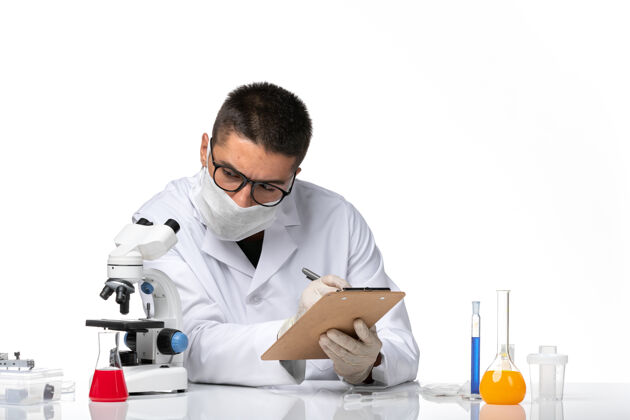 显微镜前视图穿着白色医疗服的男医生在白色空间用显微镜工作健康医生病毒