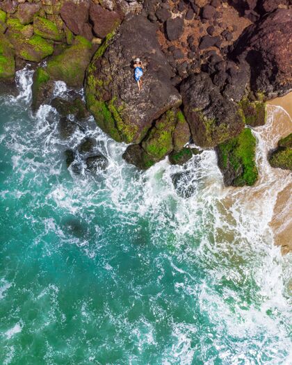 谎言一个穿着蓝色裙子躺在岩石海滩上的女性的垂直航拍女人海洋天空