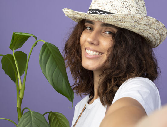 园艺微笑的年轻女园丁穿着制服戴着园艺帽手持植物穿帽子成人