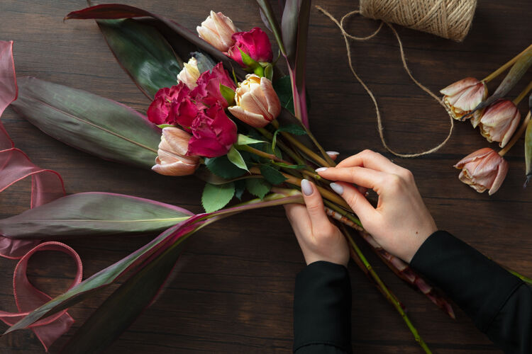 春天工作中的花匠：在木制表面上制作不同花朵的时尚现代花束的女人颜色粉彩爱