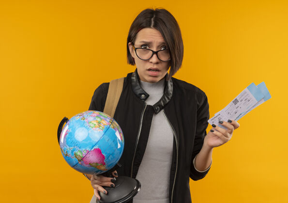 穿着给人印象深刻的年轻女学生戴着眼镜背着包拿着机票地球仪孤立在橙色飞机地球仪包