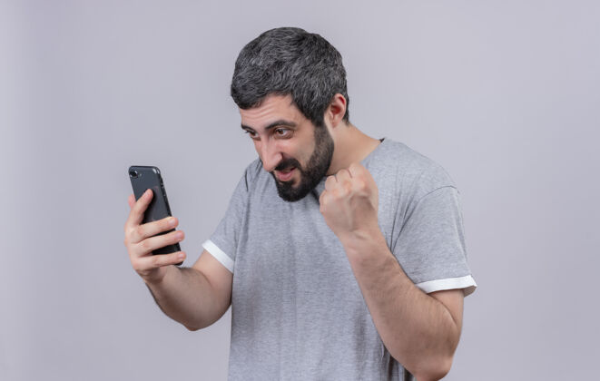 举起来快乐的年轻英俊的白人男子手持手机 看着手机 举起拳头孤立在白色拳头电话年轻