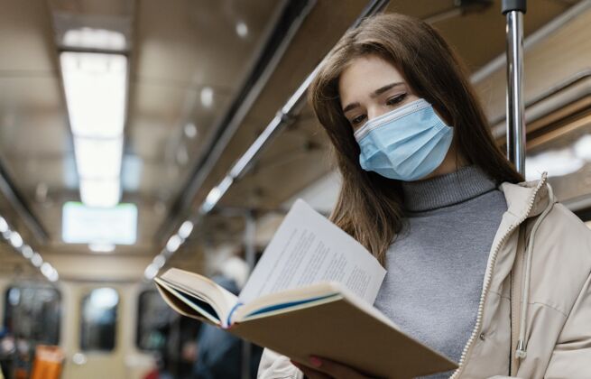 城市坐地铁读书的年轻女子外科口罩感冒读书