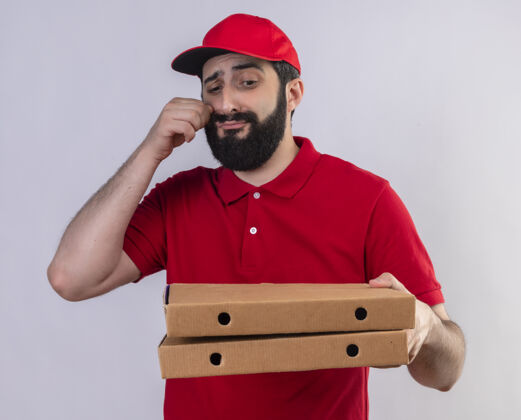 手一个年轻英俊的白人送货员 穿着红色制服 戴着帽子 看着披萨盒 手离脸很近 背景是白色的帽子不愉快帅