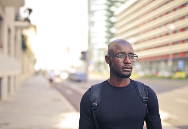 眼镜年轻的非洲男人戴着眼镜穿着黑色t恤和背包在街上自信表情背景