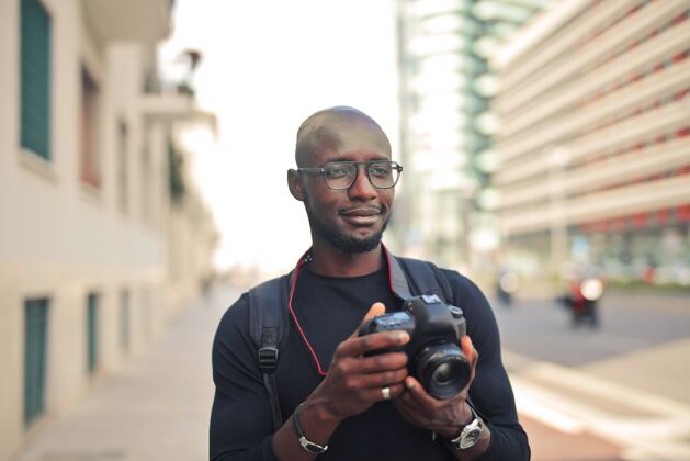 美国人年轻迷人的非洲男摄影师拿着相机在街上晒太阳记者职业设备